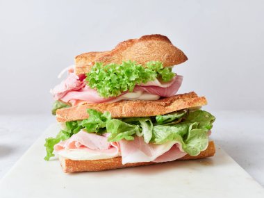 Bir sandviç taze baget, mozzarella peyniri, marul ve jambon dilimleriyle hazırlanır..