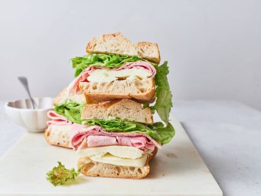 Masada baget, mozarella peyniri, jambon ve maruldan yapılmış bir yığın taze sandviç duruyor. Bu basit bir kahvaltı ya da öğle yemeği..