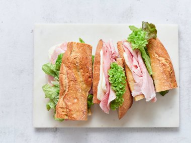 Öğle yemeğinde mozzarella, jambon ve yeşilliklerle dolu dilimlenmiş baget sandviçler var..