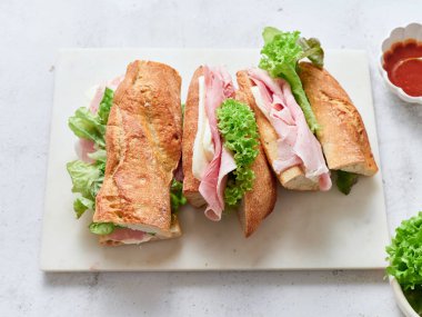 Taze hazırlanmış sandviçler dilimlenir ve masaya yerleştirilir. Peynirli, jambonlu ve marullu baget.