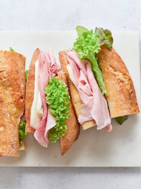 Bir yemek masasında jambon, mozzarella peyniri ve maruldan yapılmış taze sandviçler sergilenir..