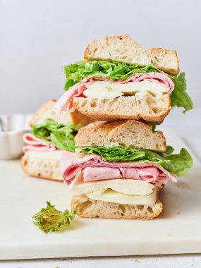 Peynirli, jambonlu ve marullu dilimlenmiş sandviçler masanın üzerinde duruyor..