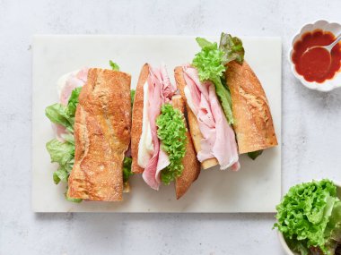 Ekmek, mozarella peyniri, marul ve jambondan yapılmış sağlıklı bir sandviç yemek masasında servis edilir.