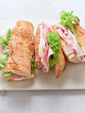 Baget, mozarella peyniri, marul ve jambondan yapılmış sandviçler mermer kesim tahtasına dizilmiştir..