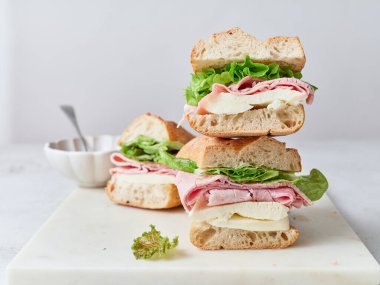Pişirilmiş ve dilimlenmiş sandviçler masaya oturur. İçindekiler baget, mozarella peyniri, jambon ve marul..
