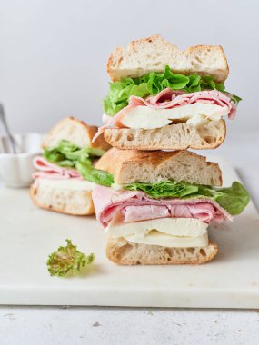 Ekmek, mozzarella peyniri, jambon ve maruldan yapılmış taze bir sandviç masada duruyor..