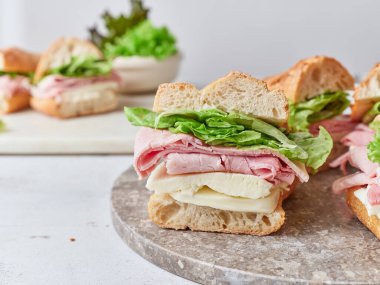 Bir yemek masasında mozzarella peyniri, jambon ve yeşil yaprak maruluyla dolu taze baget sandviçler sergilenir..