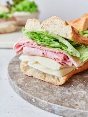 Mozarella peyniri, jambon ve marulla dolu lezzetli bir baget sandviç masada duruyor..