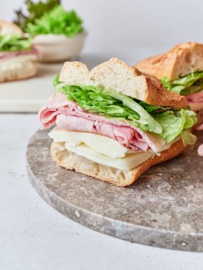 Ekmek, mozarella peyniri, jambon ve maruldan yapılmış sağlıklı bir sandviç masada oturur..