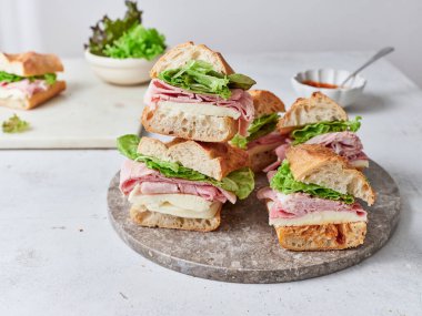 Taş bir tabakta taze yapılmış sandviçler. İçindekiler baget, mozzarella peyniri, jambon, marul ve domates sosu..