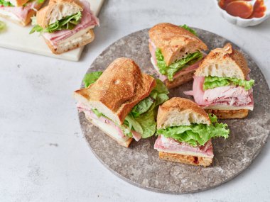 Yemek masasında jambon, peynir, marul ve domates sosuyla dolu baget sandviçler var..