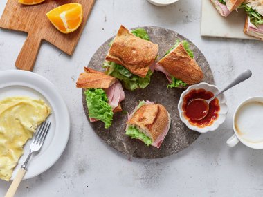 Jambonlu, mozzarellalı ve marullu taze yapılmış sandviçler dilimlenmiş portakallarla bir masaya dizilir. Domates sosu ve tereyağı da yanında servis edilir. Sabah kahvaltısı hazır..