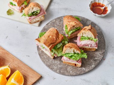 Taze yapılmış sandviçler dilimlenmiş portakallar ve küçük bir kase sosun yanında yuvarlak bir tabakta otururlar. İçindekiler arasında baget, jambon, mozzarella peyniri, marul ve domates sosu yer alıyor..