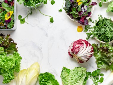 Farklı marullar, turplar, bezelyeler ve yenilebilir çiçekler mermer bir tezgahta düzenlenir. Bu kurgu, mutfakta vejetaryen yemeği ya da salata hazırlamak için..