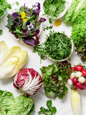 Taze marul ve sebzeler bir mutfaktaki mermer tezgahın üzerine dizilir. Sahne, canlı renkler ve dokularla yemek hazırlamak ve salata yapmak için sağlıklı seçenekler sunuyor..