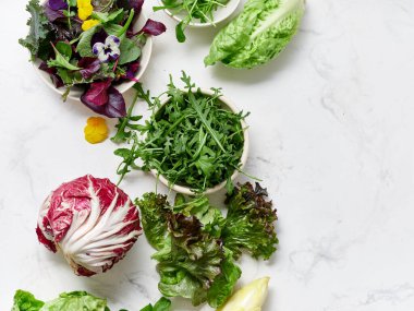 Farklı türde marul ve sebzeler bir mutfaktaki mermer tezgahın üzerinde düzenlenir. İçindekiler arasında salata yapmak için turşu, romaine, rogula ve turp vardır..