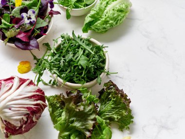 Bir mutfaktaki mermer tezgahın üzerine farklı marul koleksiyonu konur. Yeşiller salata yapmaya hazır. Sağlıklı bir yemek için ilave malzemeler de mevcuttur..