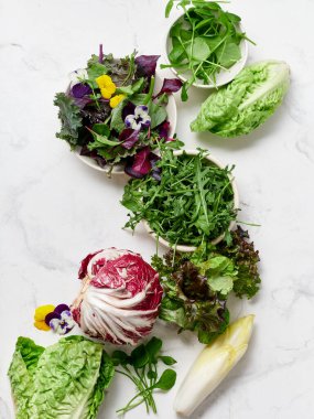 Farklı türde marul ve sebzeler bir mutfaktaki mermer tezgahın üzerinde düzenlenir. Bu düzen taze salata ve sağlıklı yemekler yapmak için ideal..