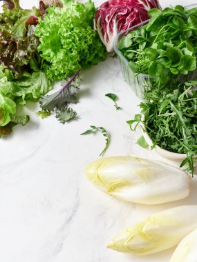 Mermer tezgahta farklı marul türleri sıralanır. Taze turp, bezelye ve yenilebilir çiçekler mevcut. Bu kurgu sağlıklı salata ve vejetaryen yemeği yapmak için..