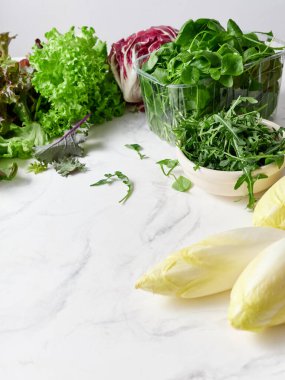 Mermer tezgah bir dizi taze marul ve sebze sergiler. Radicchio, romaine, rogula, hindiba, kırmızı yaprak ve diğer yeşiller salata hazırlığı için hazır..