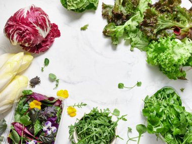 Mermer bir tezgahta farklı türde marul ve sebzeler düzenlenir. Sahnede turşu, romaine, rogula, turp ve vejetaryen yemeği için yenilebilir çiçekler var..