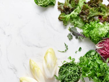 Mermer tezgahta farklı marul ve sebzeler düzenlenir. Bu ayar salata yapmak için gerekli malzemeleri gösteriyor. Turplar, bezelyeler ve yenilebilir çiçekler de dahil..