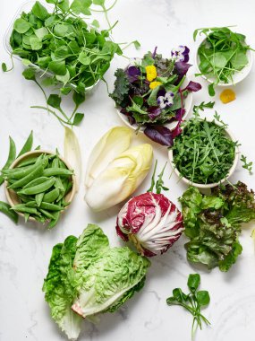 Taze marul ve sebzeler mutfaktaki mermer bir tezgahta sergilenir. Seçimde sağlıklı yemek hazırlamak için çeşitli yeşillikler ve yenilebilir çiçekler yer alıyor..