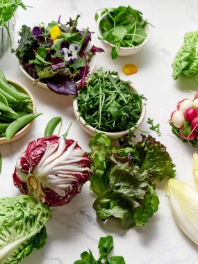 Taze marul ve sebzeler mermer tezgahta sergilenir. Çeşitli yeşillikler ve renkli eklentiler yemek hazırlığı ve salata hazırlığı için hazırdır..