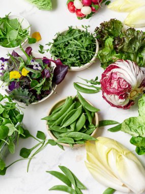 Bir mutfaktaki mermer tezgahta farklı türde marullar düzenlenir. Turplar, bezelyeler ve yenilebilir çiçekler de dahil. Hepsi sağlıklı bir vejetaryen yemeği yapmaya hazır..