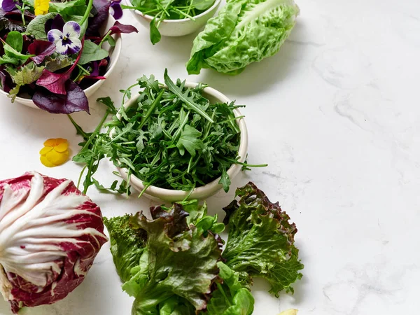 Bir mutfaktaki mermer tezgahın üzerine farklı marul koleksiyonu konur. Yeşiller salata yapmaya hazır. Sağlıklı bir yemek için ilave malzemeler de mevcuttur..