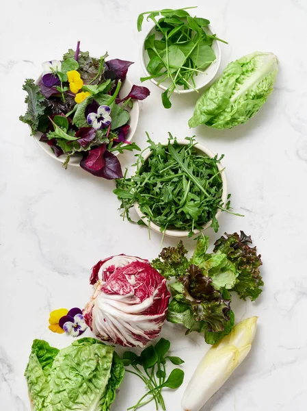 Mutfak tezgahında salata yapmak için salata ve sebze karışımı yer alır. Yeşiller, turplar, bezelyeler ve yenilebilir çiçekler vejetaryen yemeği için hazır..