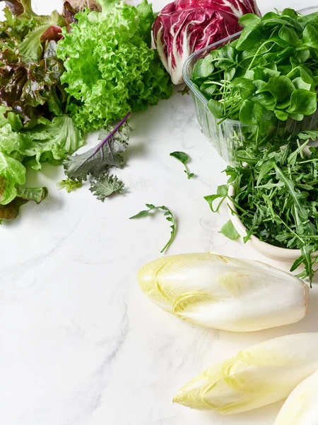 Mermer tezgahta farklı marul türleri sıralanır. Taze turp, bezelye ve yenilebilir çiçekler mevcut. Bu kurgu sağlıklı salata ve vejetaryen yemeği yapmak için..