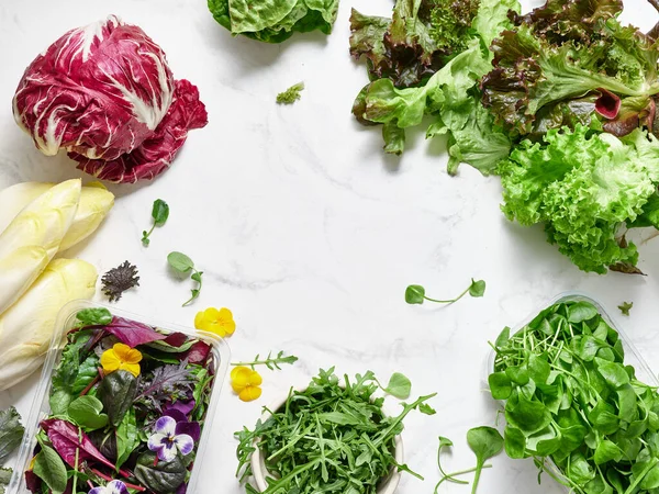 Mermer bir tezgahta farklı türde marul ve sebzeler düzenlenir. Sahnede turşu, romaine, rogula, turp ve vejetaryen yemeği için yenilebilir çiçekler var..