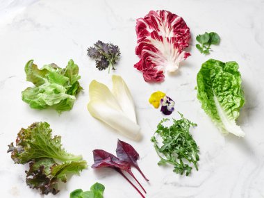 Beyaz mermer bir tezgahta, marul yaprakları ve yeşillikler bir vejetaryen yemeği için düzenlenir. Bu ekran radicchio, romaine, rogula ve yenilebilir çiçekleri içerir..