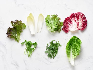 Marul yaprakları beyaz mermer bir tezgahta sergilenir. Düzenleme arasında radicchio, romaine, rogula, hindiba, kırmızı yaprak, hindiba ve yenebilir çiçeklerle karıştırılmış mesclun yer alıyor..