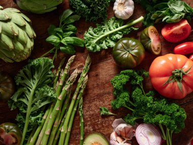 Düz bir yatak, ahşap bir yüzeyde çeşitli taze sebzelerden oluşan bir koleksiyonu gösterir. Sahnede sağlıklı beslenme ve vejetaryen yemek hazırlama, ürünlerin renkleri ve dokularıyla vurgulandı.