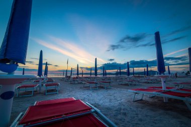 Gün batımında kumsalda güneş şemsiyeleri ve plaj sandalyeleri..