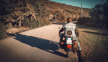 Gün batımında bir kır yolunda klasik bir motosikletli.