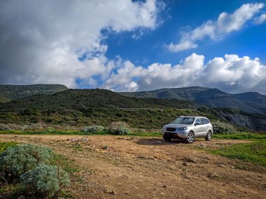 Kışın kirli bir yolda park etmiş gri bir cipin üzerinde bulutlu bir gökyüzü.