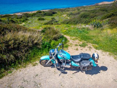 Turkuaz klasik motosiklet güneşli bir günde deniz kenarında park edilmiş.