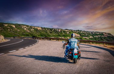 Biker on a winding road under a colorful sky at sunset