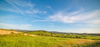 Gün batımında mavi gökyüzü altında yeşil tepeler. Sardunya, İtalya