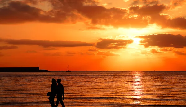 Jeune couple marchant au bord de la mer au coucher du soleil — Photo