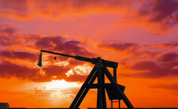 Silueta de catapulta bajo una puesta de sol roja —  Fotos de Stock