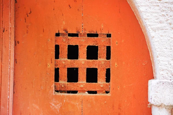 Gitter in einer alten orangefarbenen Tür — Stockfoto
