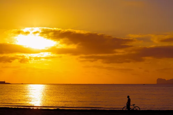 Homem com bicicleta na costa ao pôr do sol — Fotografia de Stock