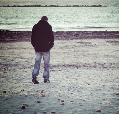Kış aylarında deniz kenarında yürüyen adam