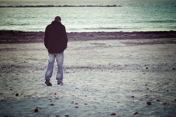 Kış aylarında deniz kenarında yürüyen adam