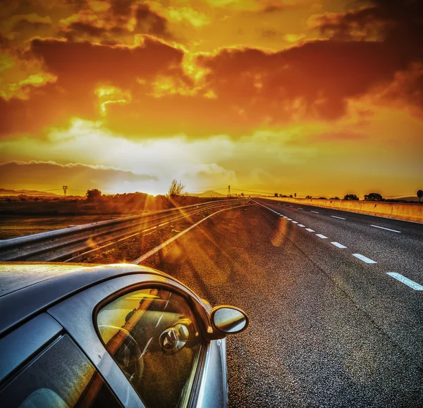 Car on the edge of the road under a scenic sky at sunset Stock Picture