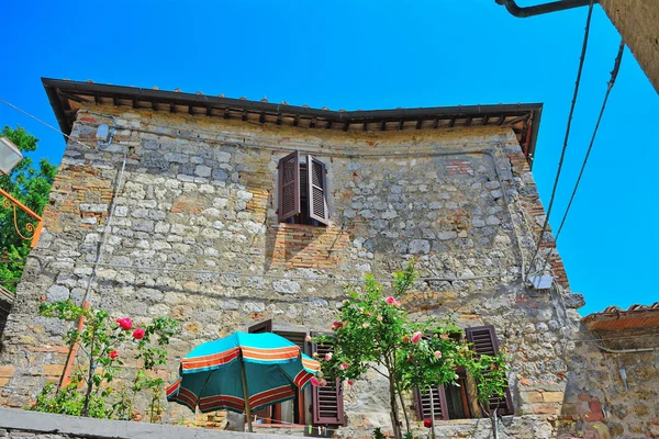 Parasol et fleurs devant un bâtiment rustique à San Gimign — Photo